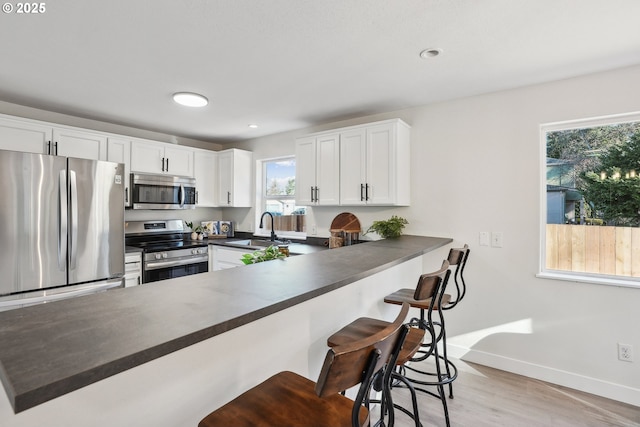 kitchen featuring stainless steel appliances, kitchen peninsula, sink, and white cabinets