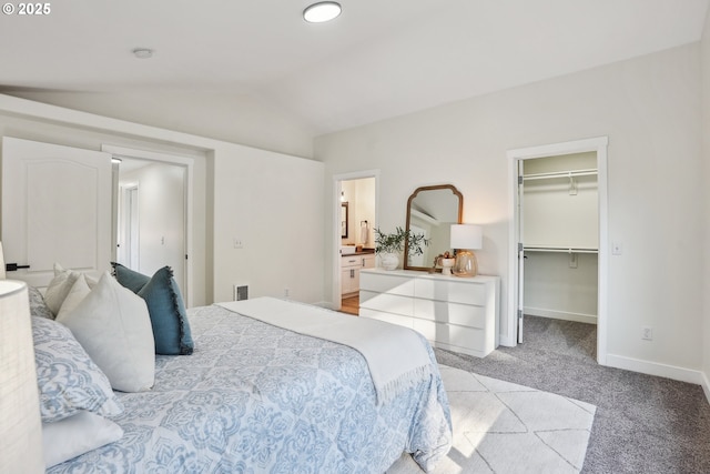 carpeted bedroom featuring a walk in closet, connected bathroom, vaulted ceiling, and a closet