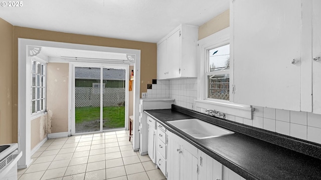 kitchen with a sink, backsplash, dark countertops, white cabinetry, and light tile patterned floors