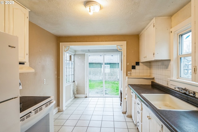 kitchen with white appliances, a sink, decorative backsplash, under cabinet range hood, and dark countertops