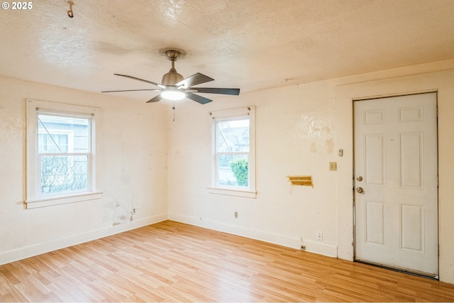 empty room with a ceiling fan, light wood-style floors, baseboards, and a textured ceiling