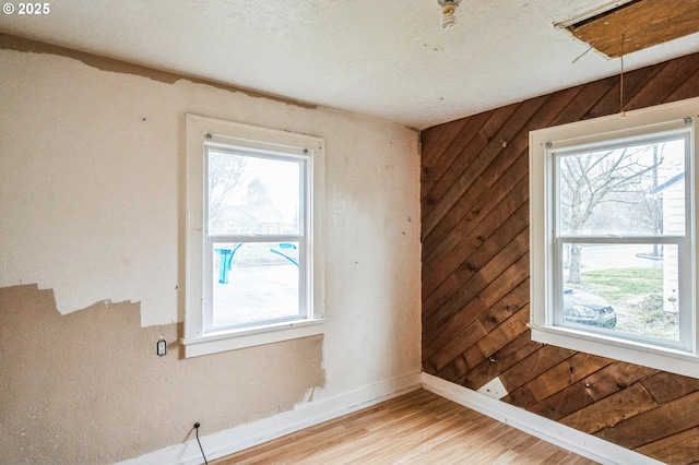 spare room with baseboards, wooden walls, a healthy amount of sunlight, and light wood finished floors