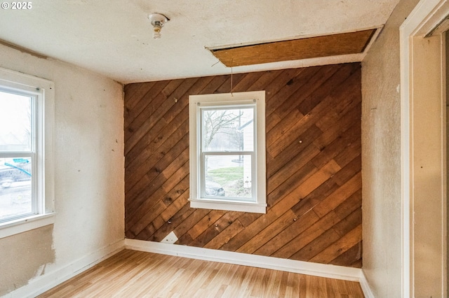 empty room featuring baseboards, wood walls, and light wood finished floors