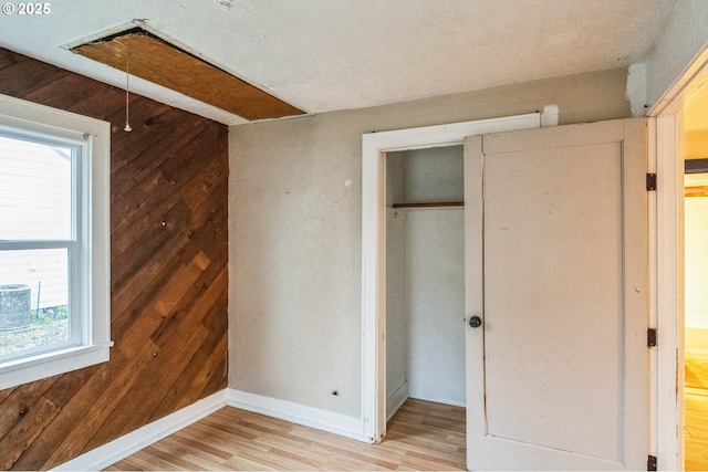 unfurnished bedroom with light wood-type flooring, baseboards, wooden walls, and a closet