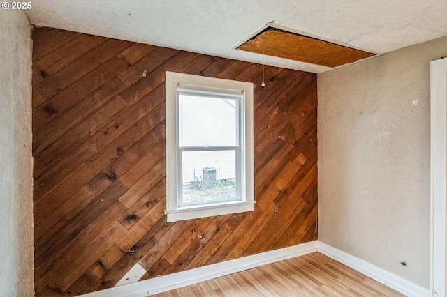 empty room featuring attic access, light wood finished floors, baseboards, and wood walls