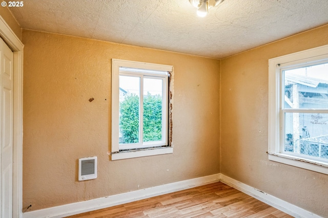 unfurnished room with a textured wall, visible vents, baseboards, and light wood finished floors