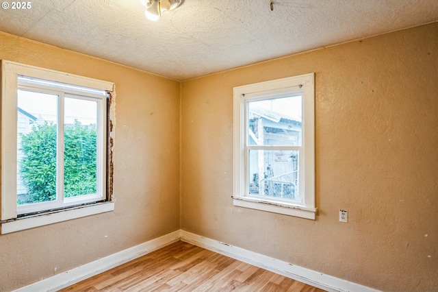 spare room with light wood-style flooring, a textured ceiling, baseboards, and a textured wall