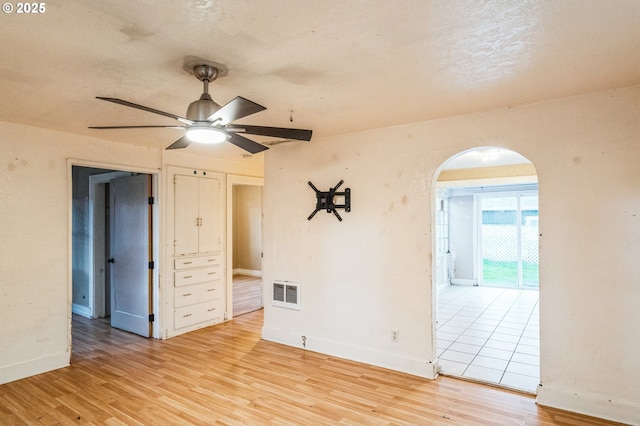 spare room with a ceiling fan, visible vents, baseboards, arched walkways, and light wood-type flooring