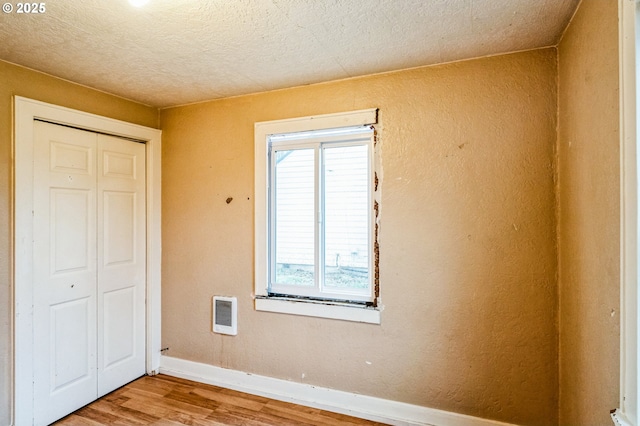 unfurnished bedroom featuring wood finished floors, visible vents, baseboards, a closet, and a textured wall