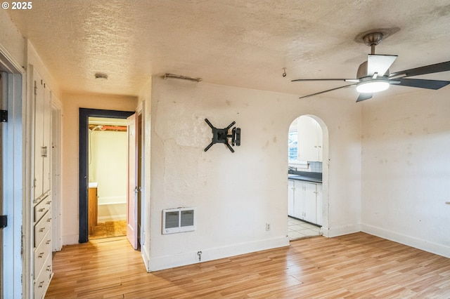 empty room with visible vents, light wood-style flooring, arched walkways, a textured ceiling, and a ceiling fan