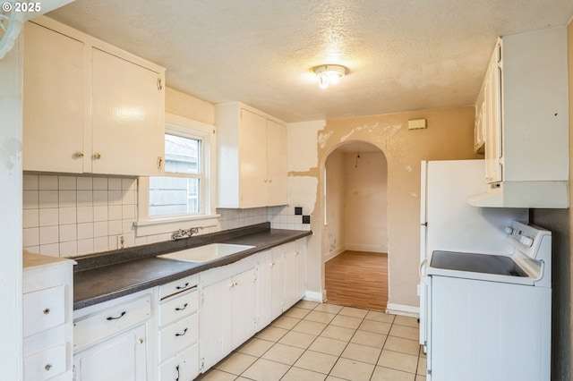 kitchen with dark countertops, arched walkways, washer / clothes dryer, and a sink