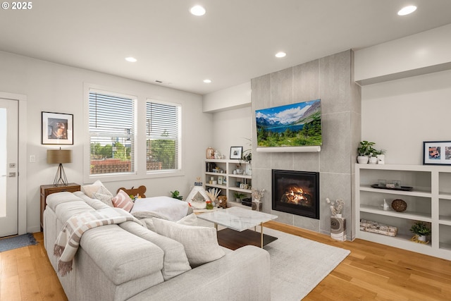 living room featuring recessed lighting, a tiled fireplace, and light wood-type flooring