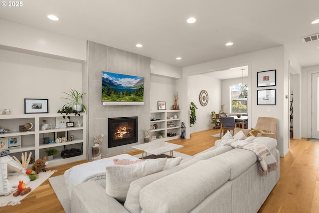 living area with light wood finished floors, a tiled fireplace, built in shelves, recessed lighting, and visible vents