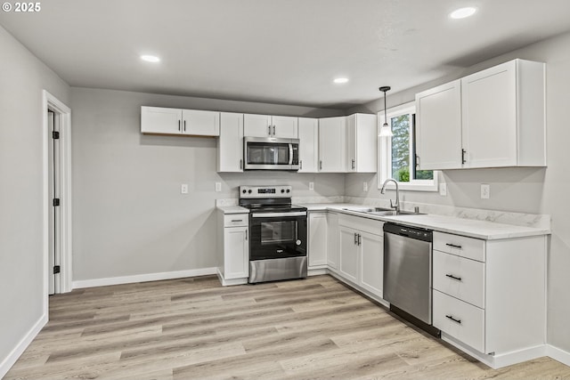 kitchen with white cabinetry, light hardwood / wood-style floors, appliances with stainless steel finishes, pendant lighting, and sink