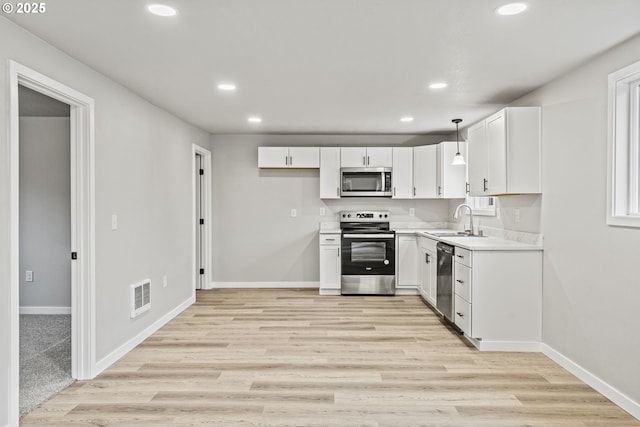 kitchen featuring decorative light fixtures, sink, light wood-type flooring, appliances with stainless steel finishes, and white cabinets