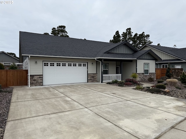 view of front facade featuring a porch, a shingled roof, an attached garage, stone siding, and driveway