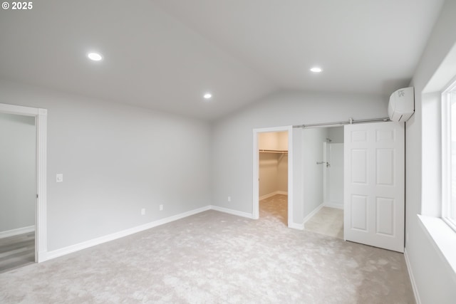 unfurnished bedroom with light carpet, a barn door, lofted ceiling, a walk in closet, and a wall mounted AC