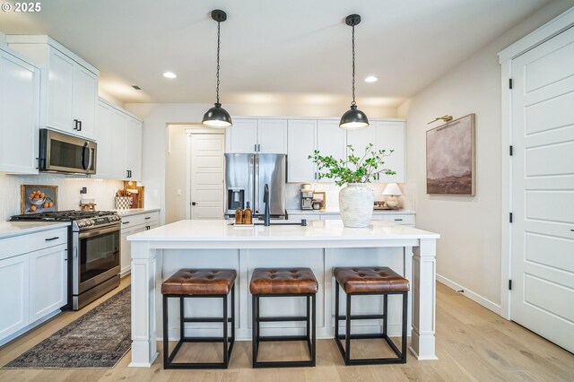 kitchen featuring stainless steel appliances, light hardwood / wood-style floors, a kitchen island with sink, and white cabinets