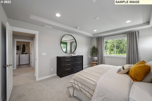 bedroom featuring independent washer and dryer, a tray ceiling, and light carpet