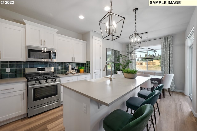 kitchen with appliances with stainless steel finishes, an island with sink, sink, white cabinets, and light hardwood / wood-style flooring