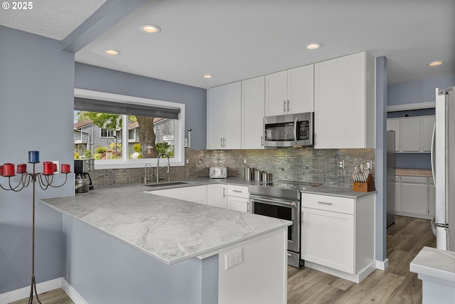 620 N Hayden Bay Dr, Portland, OR 97217 - kitchen with appliances with stainless steel finishes, a sink, white cabinetry, a peninsula, and decorative backsplash