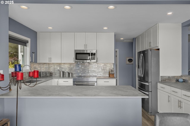 620 N Hayden Bay Dr, Portland, OR 97217 - kitchen with appliances with stainless steel finishes, a peninsula, backsplash, white cabinets, and recessed lighting