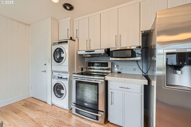 1805 NE Saratoga St, Portland, OR 97211 - kitchen with stainless steel appliances, stacked washer / drying machine, under cabinet range hood, light wood-style flooring, and tasteful backsplash