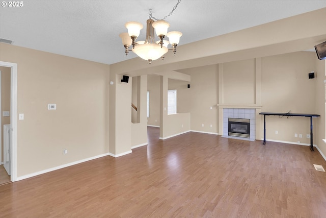 unfurnished living room featuring a chandelier, wood finished floors, a tile fireplace, and baseboards