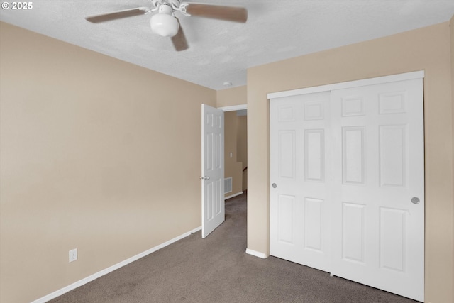 unfurnished bedroom with dark colored carpet, baseboards, a closet, ceiling fan, and a textured ceiling