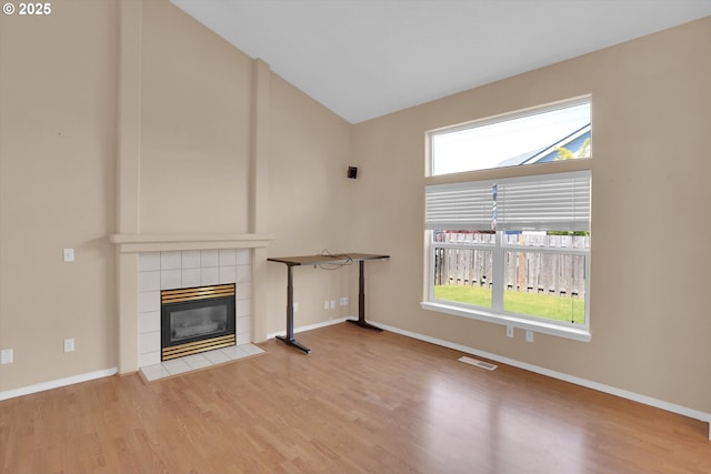 unfurnished living room featuring a fireplace, wood finished floors, baseboards, and high vaulted ceiling