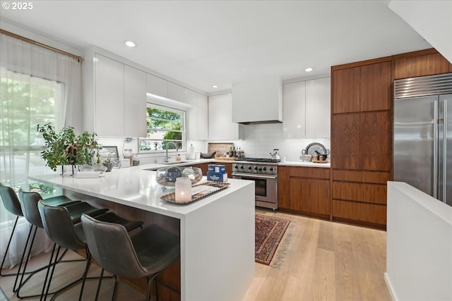 7338 N Chase Ave, Portland, OR 97217 - kitchen with high end appliances, light wood-type flooring, a kitchen bar, white cabinetry, and decorative backsplash