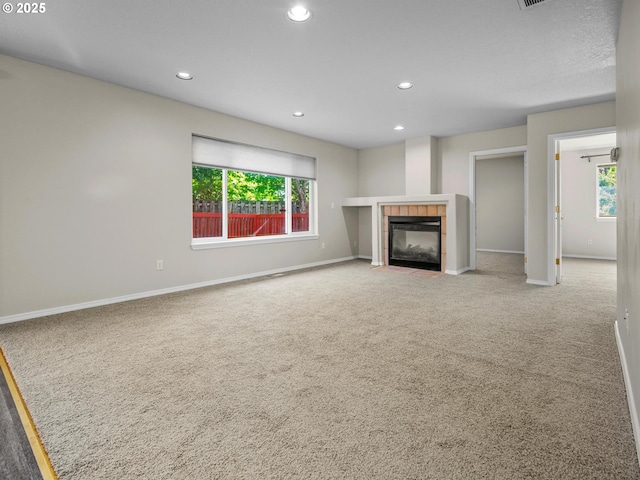 unfurnished living room with a wealth of natural light, a tile fireplace, and carpet flooring