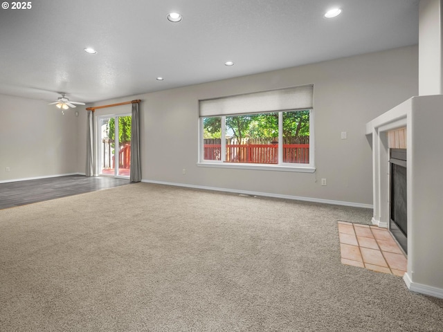 unfurnished living room with a tile fireplace, light carpet, and ceiling fan