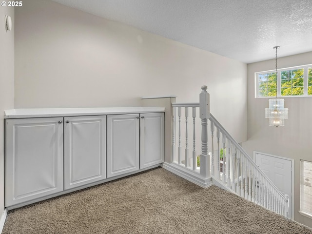 hallway featuring an inviting chandelier, light colored carpet, and a textured ceiling