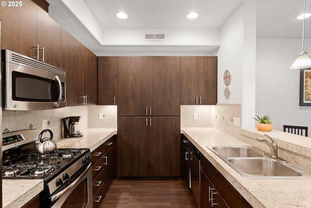 kitchen with appliances with stainless steel finishes, a sink, dark wood-type flooring, light countertops, and dark brown cabinets
