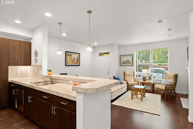 kitchen featuring a sink, a peninsula, dark wood-style flooring, light countertops, and dishwasher
