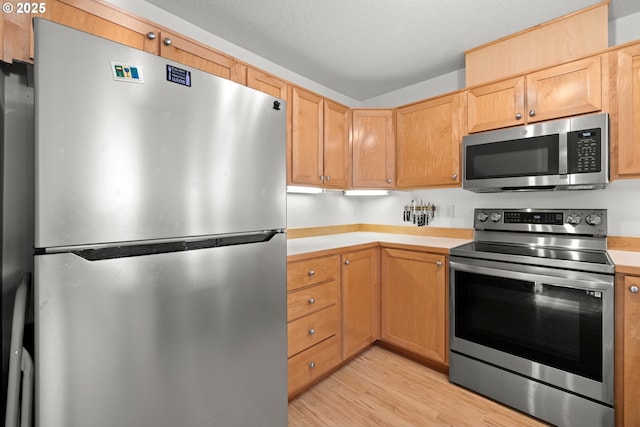 kitchen featuring stainless steel appliances, light wood-type flooring, light countertops, and a textured ceiling