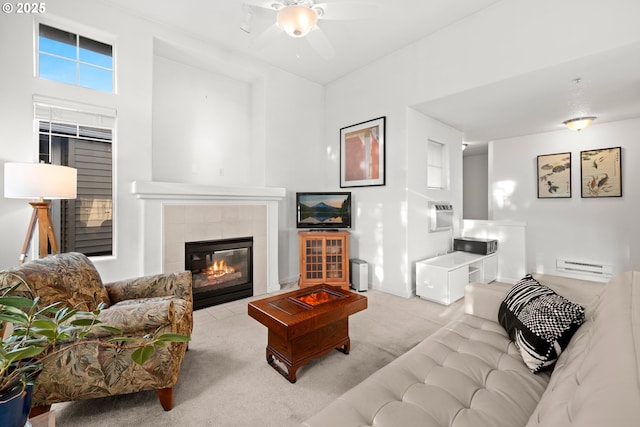 carpeted living room featuring a baseboard radiator, ceiling fan, and a tiled fireplace