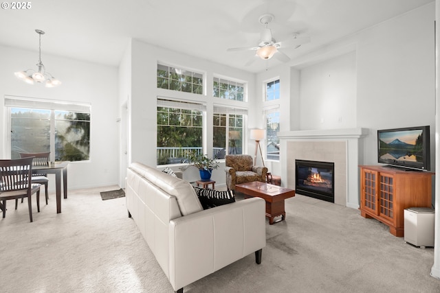 carpeted living room featuring ceiling fan with notable chandelier and a tiled fireplace