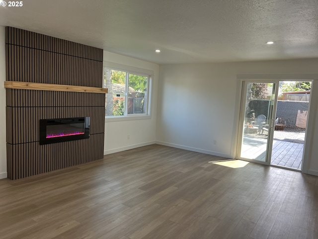 unfurnished living room with wood finished floors, recessed lighting, baseboards, a glass covered fireplace, and a textured ceiling
