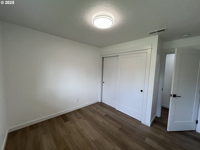 unfurnished bedroom featuring a textured ceiling, dark wood-type flooring, baseboards, and a closet
