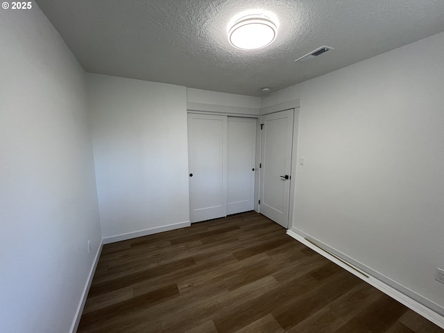 spare room with a textured ceiling, dark wood-type flooring, and baseboards