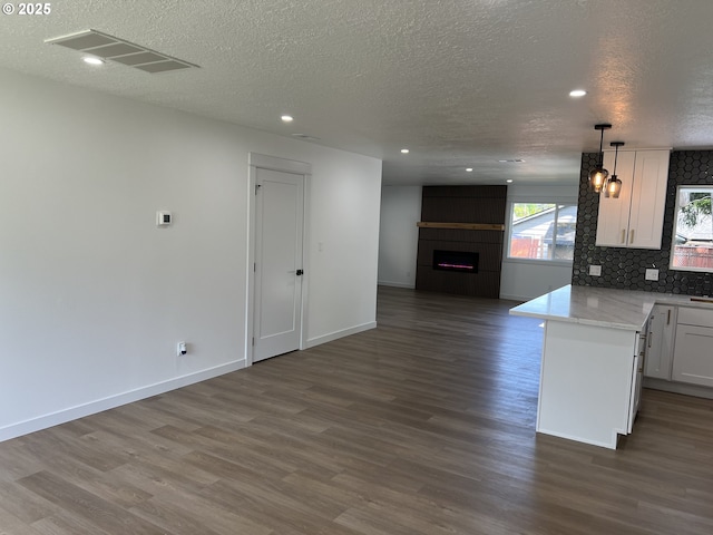 kitchen featuring open floor plan, a textured ceiling, a large fireplace, dark wood-style flooring, and white cabinets