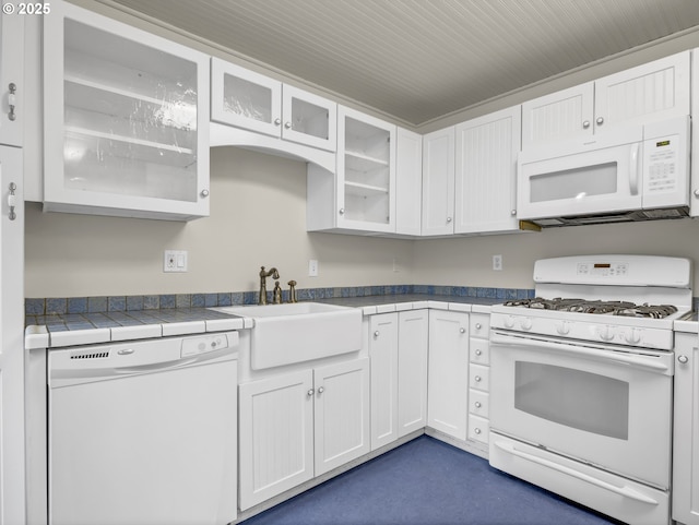 kitchen with white appliances, white cabinets, a sink, glass insert cabinets, and tile countertops