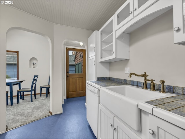 kitchen with tile countertops, white cabinets, a sink, and glass insert cabinets