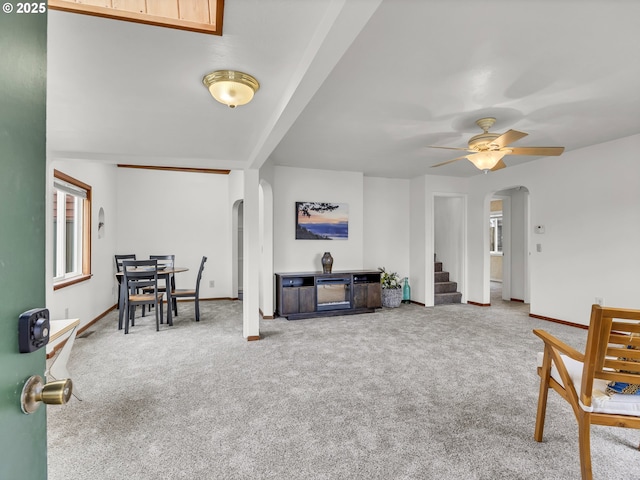 living room featuring arched walkways, carpet floors, stairs, and a ceiling fan