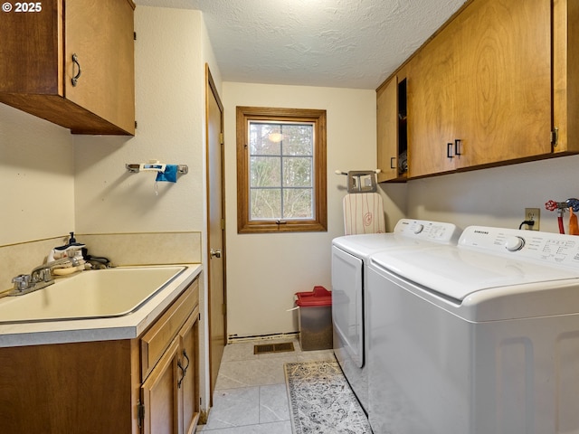 laundry room featuring light tile patterned floors, cabinet space, washing machine and dryer, a sink, and a textured ceiling