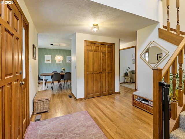 foyer featuring visible vents, light wood-style flooring, stairway, a textured ceiling, and baseboards