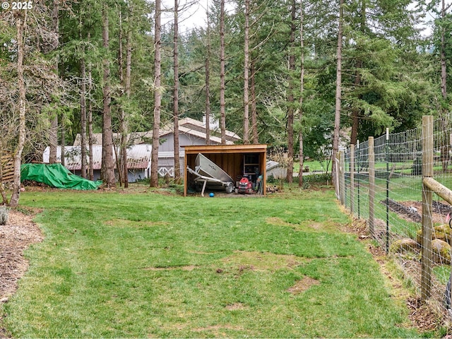 view of yard with an outbuilding, a wooded view, and fence