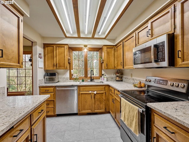 kitchen with light tile patterned floors, brown cabinetry, appliances with stainless steel finishes, light stone counters, and a sink